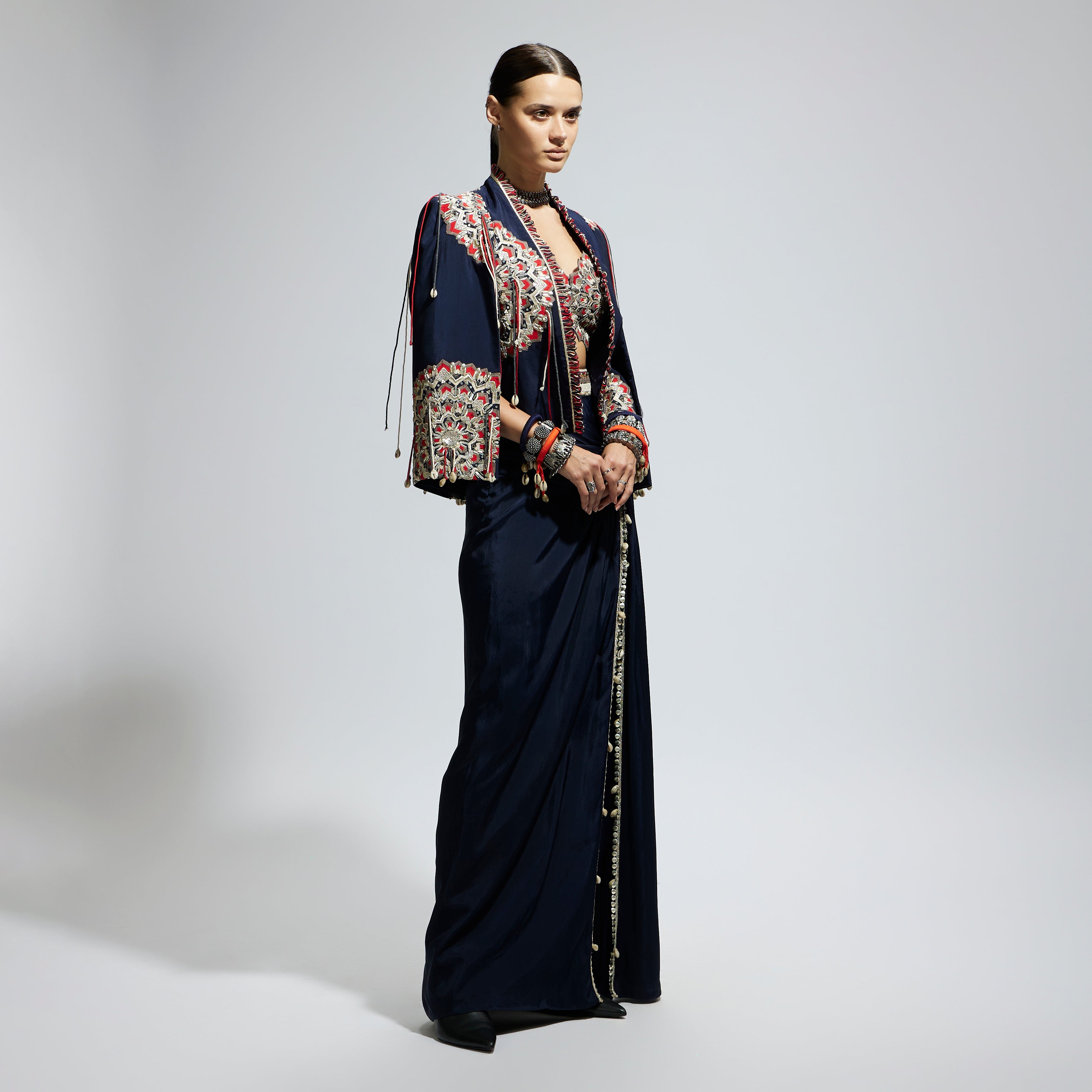 BLUE ASYMETRIC THREADWORK CAPE JACKET PAIRED WITH AN EMBELLISHED BUSTIER AND HIGH SLIT SKIRT