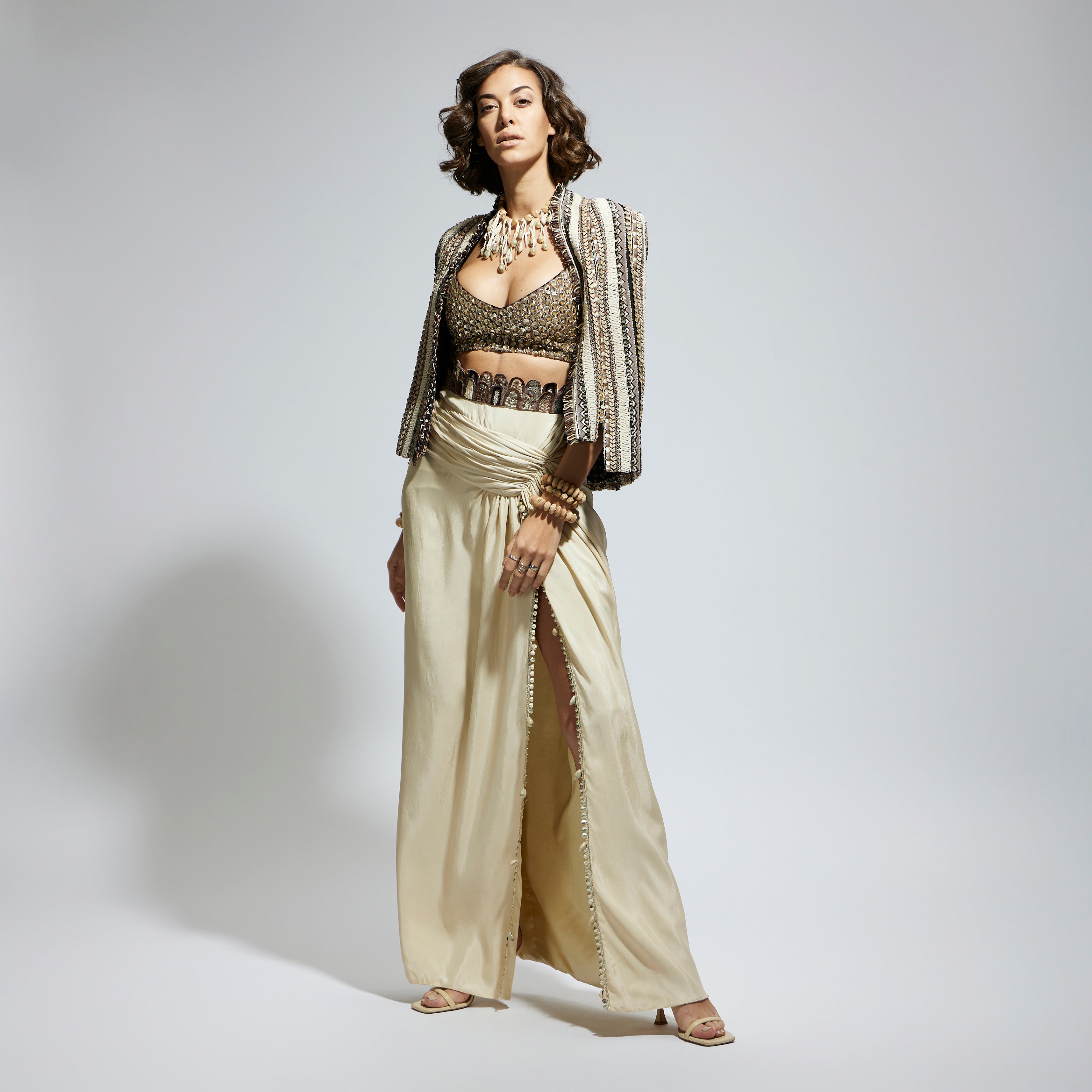 SAMSARA: EMBELLISHED & TEXTURED CAPE JACKET PAIRED WITH METALLIC SCALLOP BUSTIER AND IVORY HIGH SLIT SKIRT