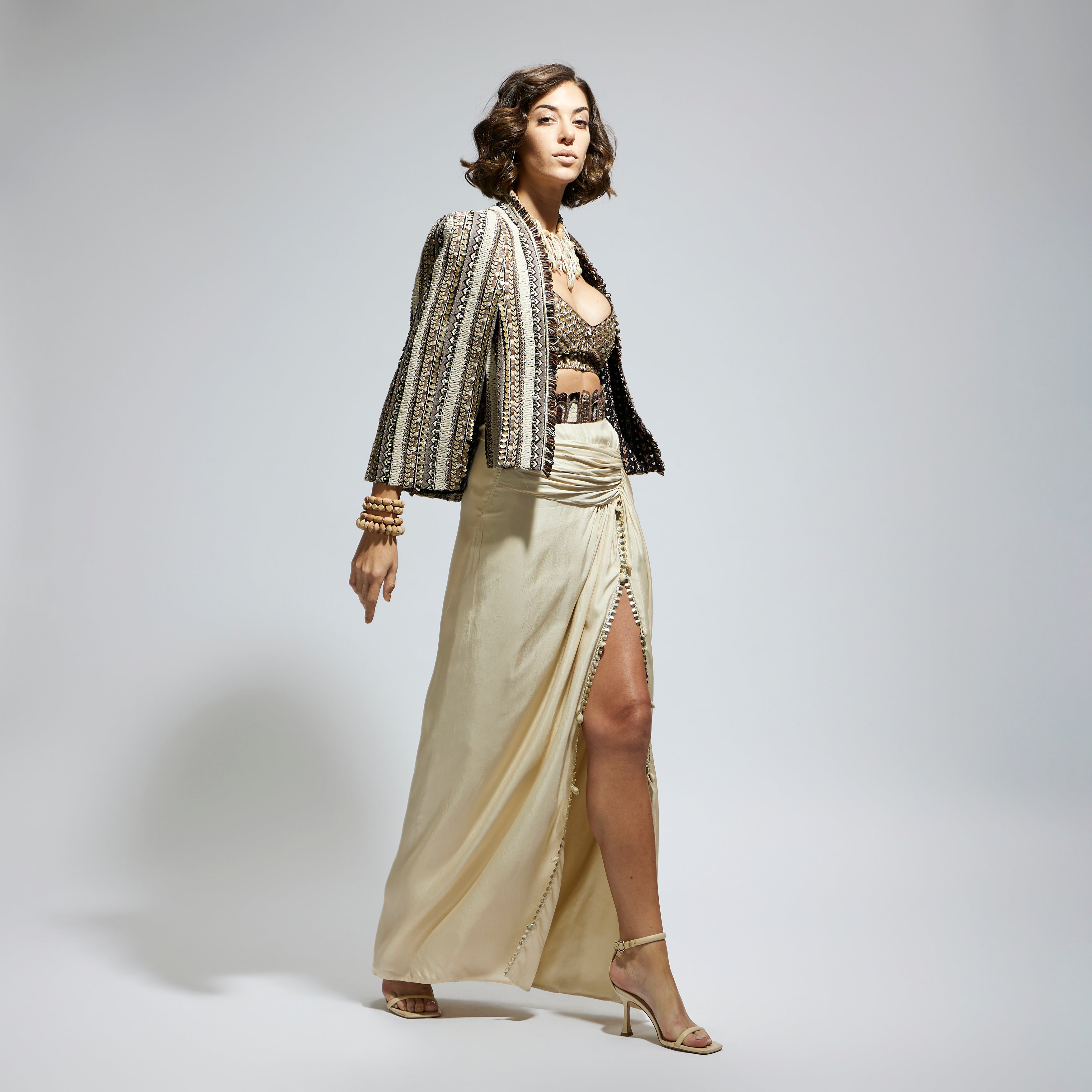 EMBELLISHED & TEXTURED CAPE JACKET PAIRED WITH METALLIC SCALLOP BUSTIER AND IVORY HIGH SLIT SKIRT