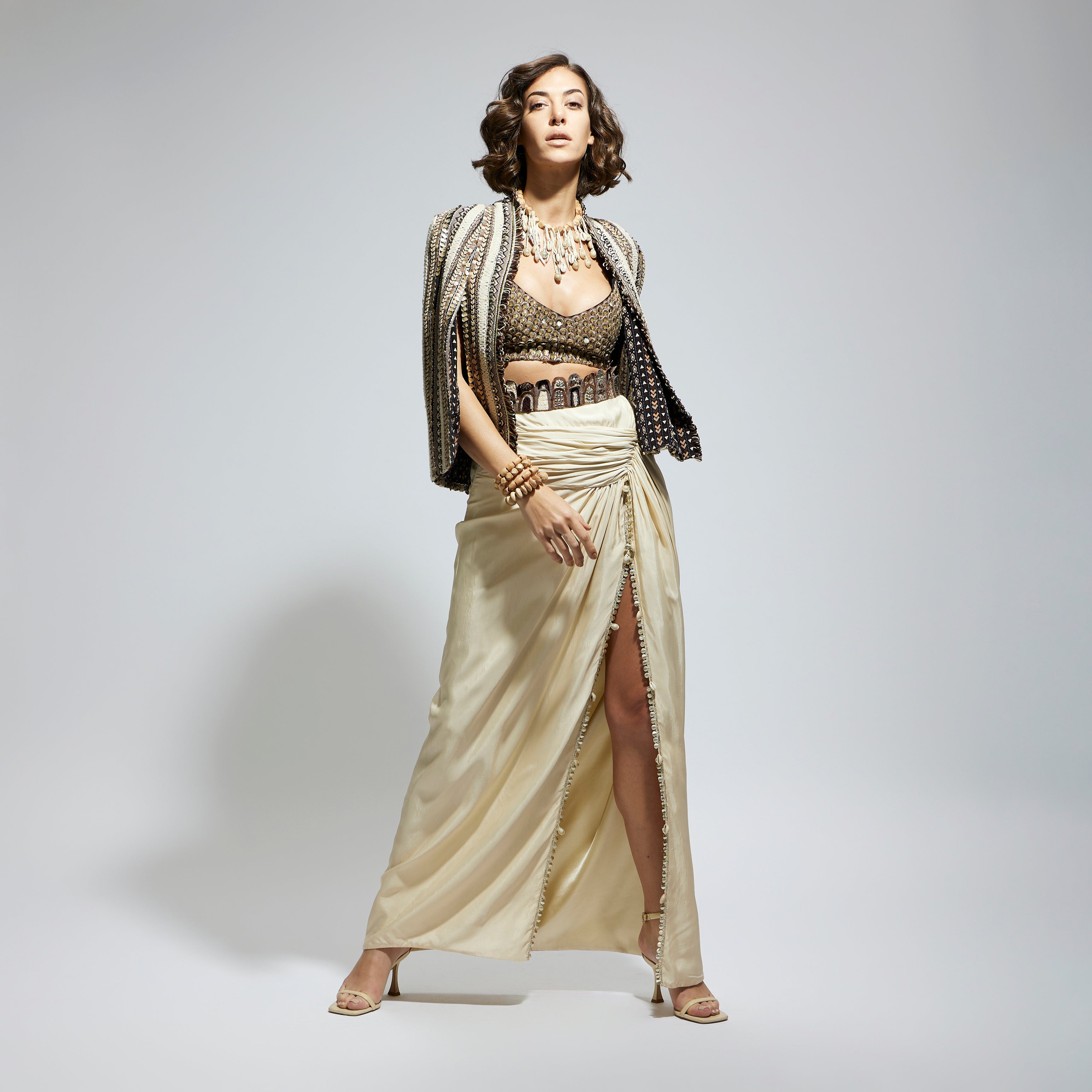 EMBELLISHED & TEXTURED CAPE JACKET PAIRED WITH METALLIC SCALLOP BUSTIER AND IVORY HIGH SLIT SKIRT